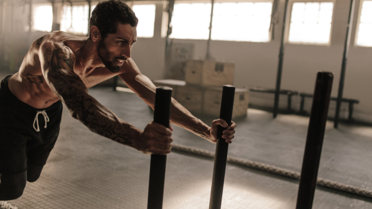 shirtless person pushing weighted sled in gym