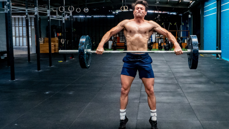 Person in gym performing barbell Olympic lift.