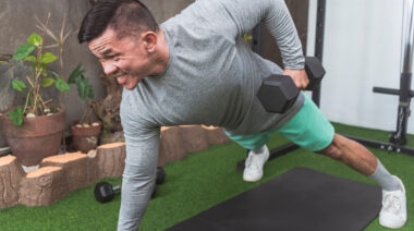 Muscular person in outdoor gym doing dumbbell row exercise on floor