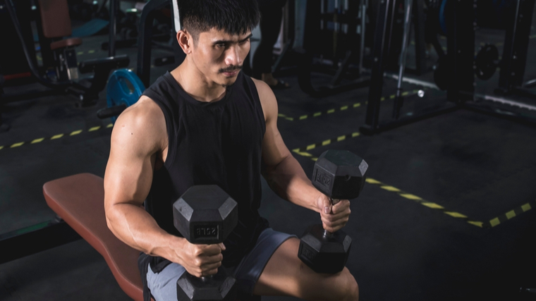 man in gym sitting on bench ready to lift dumbbells