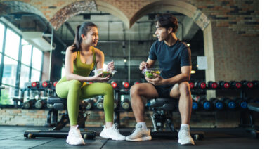 Two people sitting in gym eating food