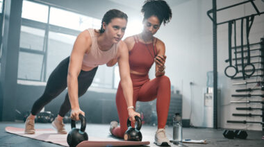 Personal trainer watching client exercise with kettlebells in gym