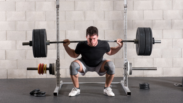 person in gym doing heavy barbell squat